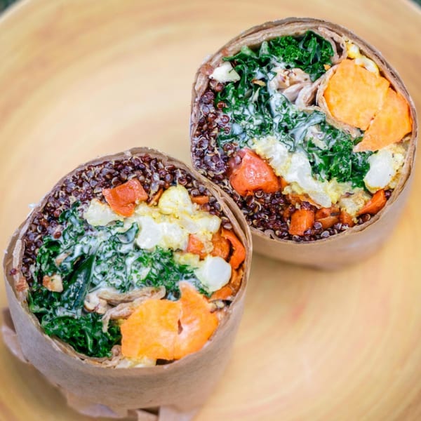 Two healthy wraps, cut in half, filled with quinoa, kale, sweet potato, and a creamy dressing.