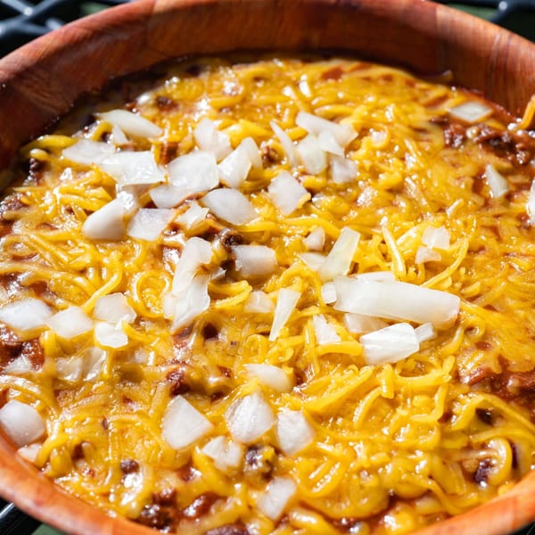 Close-up of chili with melted shredded cheese and diced white onions in a wooden bowl.
