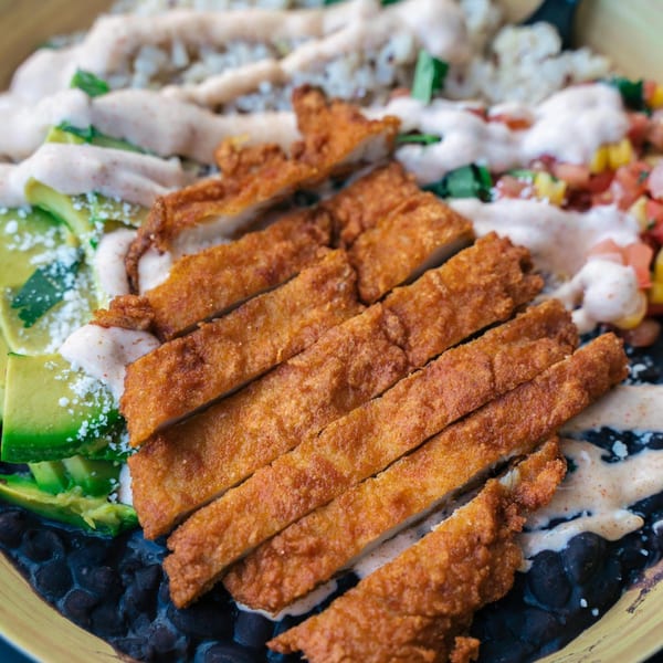 Close-up of a healthy bowl with crispy chicken, black beans, avocado, and creamy sauce.