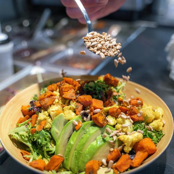 A healthy salad with greens, avocado, roasted sweet potatoes, and cauliflower, topped with sunflower seeds.