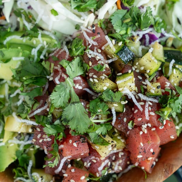 Close-up of a healthy poke bowl with tuna, avocado, zucchini, cilantro, and sesame seeds.