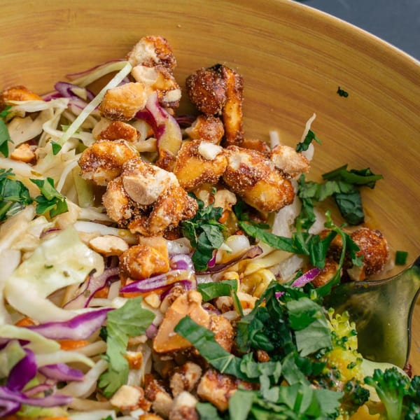 Close-up of a healthy salad with crispy chicken, shredded cabbage, and fresh herbs in a wooden bowl.